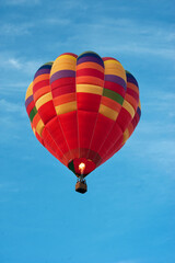 A colorful bright hot air balloon in the blue sky with a fire in the basket heating the air in the dome