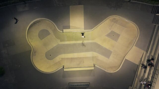 Aerial footage of a skater performing tricks inside a modern skatepark bowl at night.