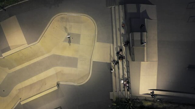 Aerial footage of a skater performing tricks inside a modern skatepark bowl at night.