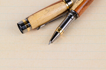 Fototapeta premium elegant wooden pens with natural grain patterns and brass and metal accents, placed on an open notebook with blank cream-colored pages, ideal for writing, office, and creative projects. 