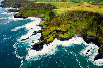 Dramatic Aerial of Giant’s Causeway Cliffs With Crashing Blue Waves During a Cloudy Day