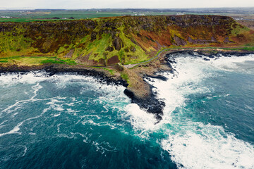 Moody Aerial View of Giant’s Causeway With Waves Crashing Into the Rocks and People Walking Around	