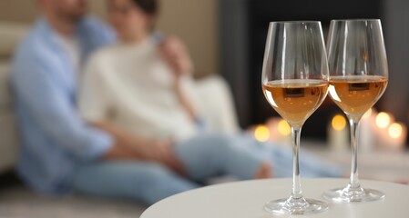 Couple near fireplace at home, focus on glasses of wine