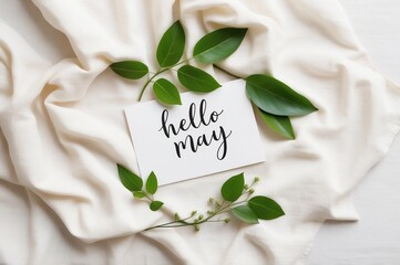 hello may card surrounded by green leaves on a soft white fabric