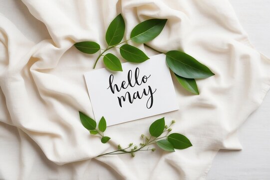 hello may card surrounded by green leaves on a soft white fabric - Powered by Adobe