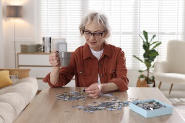 Woman with cup of drink solving jigsaw puzzle at wooden table indoors