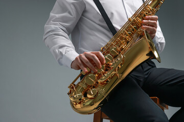 Obraz premium Professional musician playing saxophone on grey background, closeup
