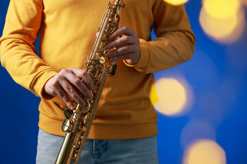 Professional musician holding soprano saxophone on blue background with blurred lights, closeup....