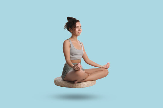 Young woman levitating during meditation on light blue background. Practicing yoga