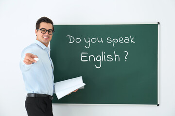 Teacher near green chalkboard with phrase Do You Speak English? in classroom