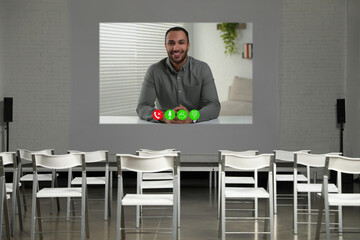 Speaker participating in lecture via online video chat. Empty conference room with projection...
