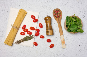 Wooden bowl with spinach, cherry tomatoes on a wooden plate, spoon with spices, uncooked spaghetti tied with twine
