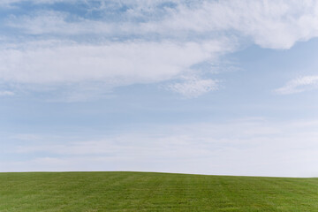 A lush green meadow stretches under a vast blue sky, showcasing fluffy clouds. The serene landscape invites tranquility and peace of mind.