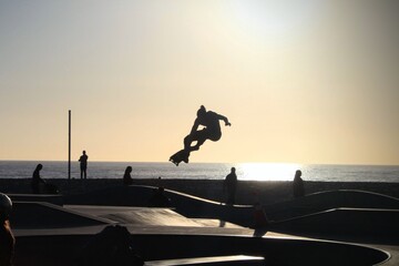 Silhouette of a skateboarder mid-jump at a Venice Beach, California skate park during golden hour © Evelyn Marie