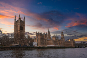 Fototapeta premium The Palace of Westminster with the Elizabeth Tower and Big Ben, set against a vibrant sunset sky, reflected on the River Thames in London, England.
