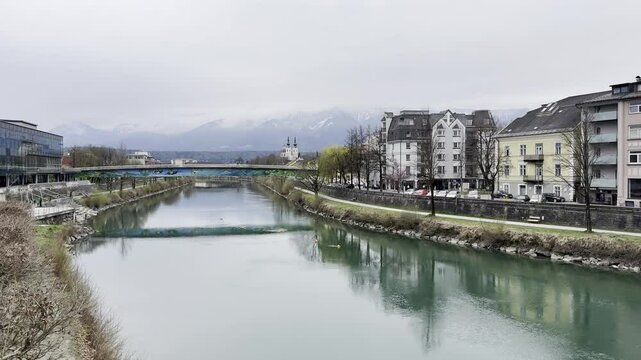 Tranquil river scene with city Villach landscape and snowcapped mountains on overcast day