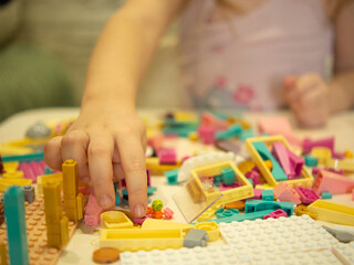 A young teenage girl assembles a construction set from plastic parts and blocks with her hands.