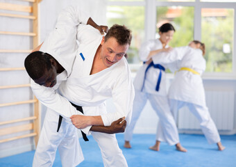 Judo or jiu-jitsu classes - two men practicing grabbing and throwing on sports mats under the...
