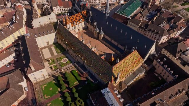 Ornate roof tiles cover old Beaune hospice in France. Aerial drone video