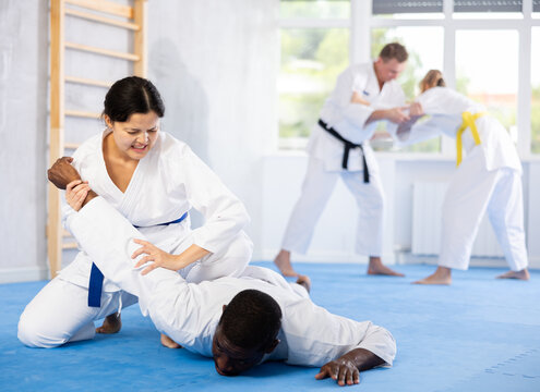 Adult man and young woman judokas practicing judo technique in group in gym