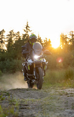 Driver riding motorcycle on gravel road during sunset, spring mountains