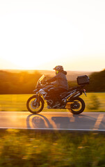 Obraz premium Driver riding motorcycle on empty road during sunset, spring mountains