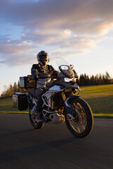 Naklejka premium Driver riding motorcycle on empty road during sunset, spring mountains
