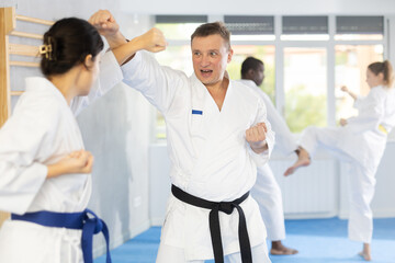 Adult man and young woman judokas practicing judo technique in group in gym