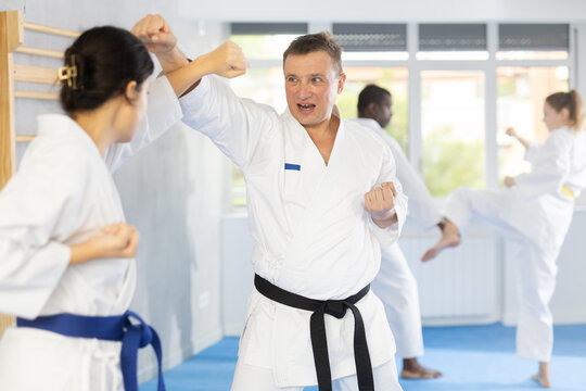 Adult man and young woman judokas practicing judo technique in group in gym