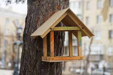 A handmade wooden birdfeeder mounted on a park tree, covered in colorful accents; ideal for...