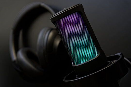 Stylish RGB microphone with headphones on dark background, perfect for illustrating streaming or podcasting setups. Photo