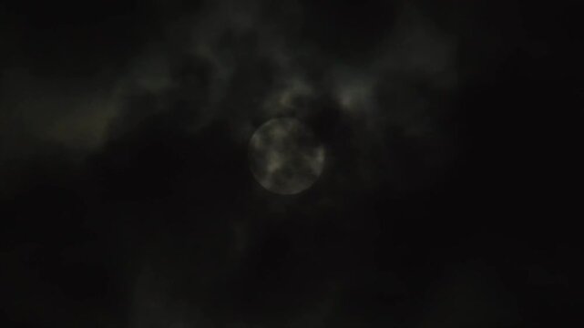 Full moon on a dark night with clouds flying in front of the moon like in thrillers and horror movies. Real shot of black night cloudy sky with moon
