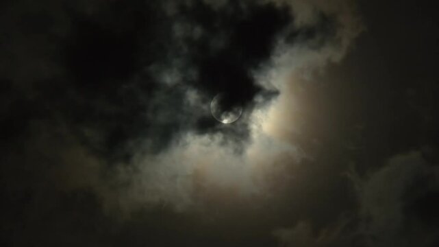 The moon in the night sky shines brightly behind the clouds. Close-up of the skyscape at midnight. Clouds fly in front of the full moon