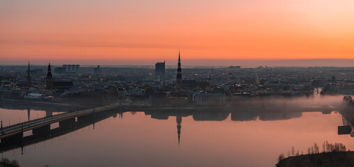 Serene sunrise over Riga, Latvia, featuring St. Peter's Church spire, historic buildings, a bridge...