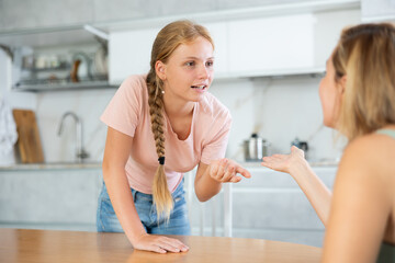 Smiling teenage girl engrossed in lively friendly conversation with woman at home kitchen. Concept of close and trusting relationships between daughter and mother
