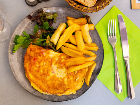 Roasted omelet served with french fries and salad on a ceramic plate in a restaurant