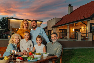 Family enjoying dinner together in the backyard of their house during sunset