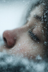 Fototapeta premium close-up winter portrait of young woman lying in snow, peaceful emotional expression with soft flakes and cold seasonal textures, serene outdoor scene capturing natural beauty and introspection