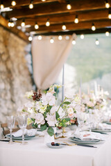 Bouquet of flowers stands on a festive table on a terrace with glowing garlands