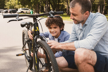 Closeup portrait of cheerful dad and son fixing bike using wire cutter at public park