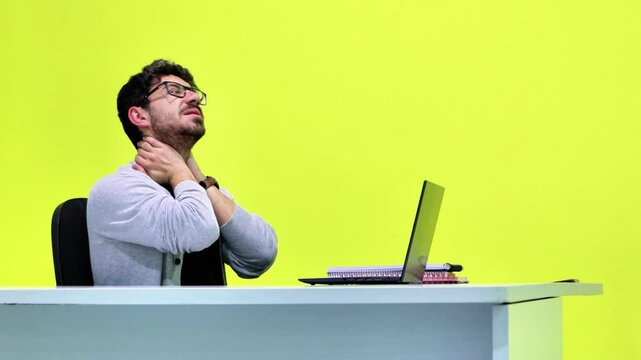 Office worker stretching neck at desk on yellow background