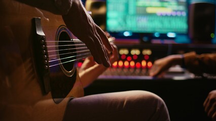 Fototapeta premium Skilled composer producing and recording new track on guitar, creating a live performance in control room. Songwriter artist composing music for his new album. Close up. Camera B.