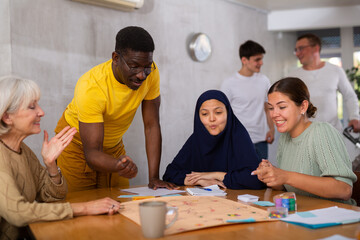 Portrait of cheerful adult african american man playing interesting board game with friends at home