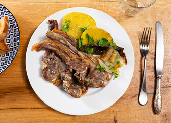 Dish from chef of restaurant is barbecue lamb ribs garnished with baked potatoes, peppers, onions. Vegetables sprinkled with chopped herbs and drizzled with olive oil