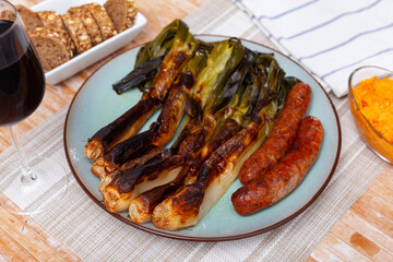 Plate of classic Catalan festive winter dish of grilled calcots with savory butifarra sausage and side of spicy homemade romesco sauce served on plate linen placemat