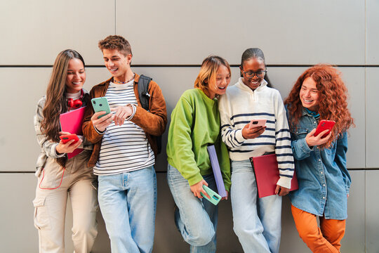 Group of cheerful teens using their smartphones while enjoying together, sharing on the social media as they communicate through various applications and features on their mobile phone