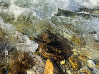 dynamic flow of crystal clear transparent river water over assorted colorful stones. raw nature...
