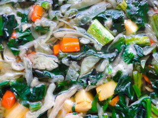 Broth with carrots, onions various fresh vegetables in a pot - colorful fresh clear spring soup. Rural kitchen scenery vegetarian bouillon or stock