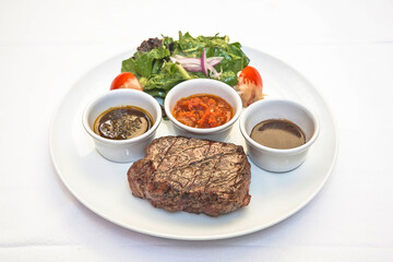 Grilled beef steak with lettuce salad and spicy sauces, plate of sliced ​​roast beef with salad and tomato on a white background