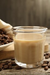 Coffee cream liqueur in glass and beans on wooden table, closeup
